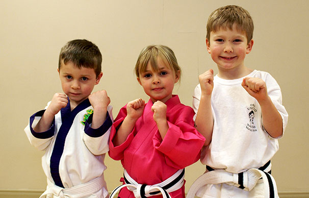 Three children stand together with their fists raised. There are two boys and the girl is in the middle of them. The two children on the left are focused as the boy on the right smiles widely.